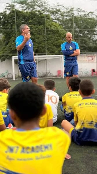 Professores da JW7 conversando com os atletas sentados no campo antes do treino
